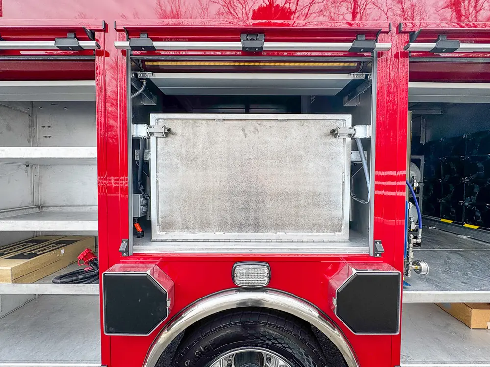 Exterior view of small fire truck showing cab, body compartments, and wheel/tire area.