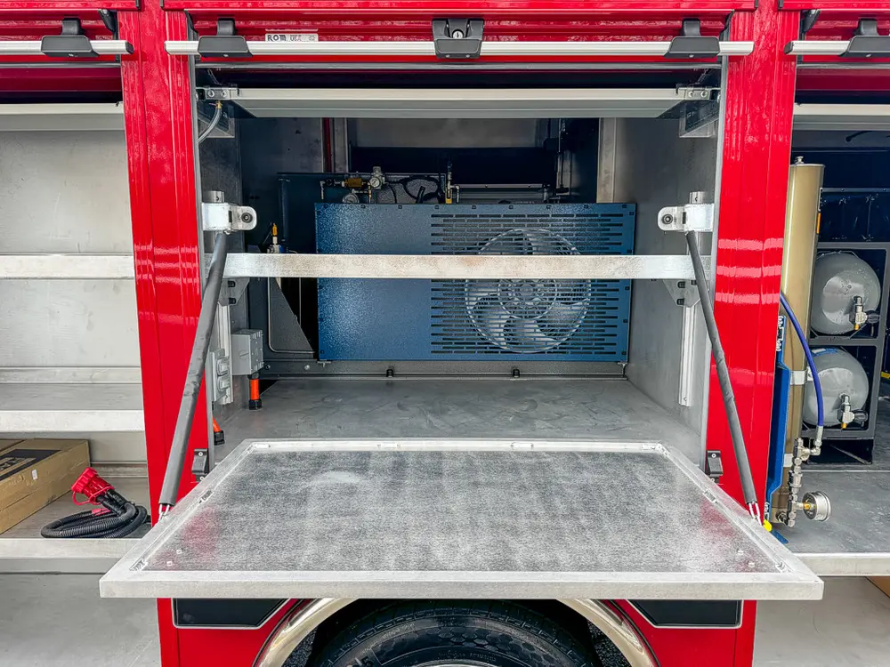 Exterior view of small fire truck showing cab, body compartments, and wheel/tire area.