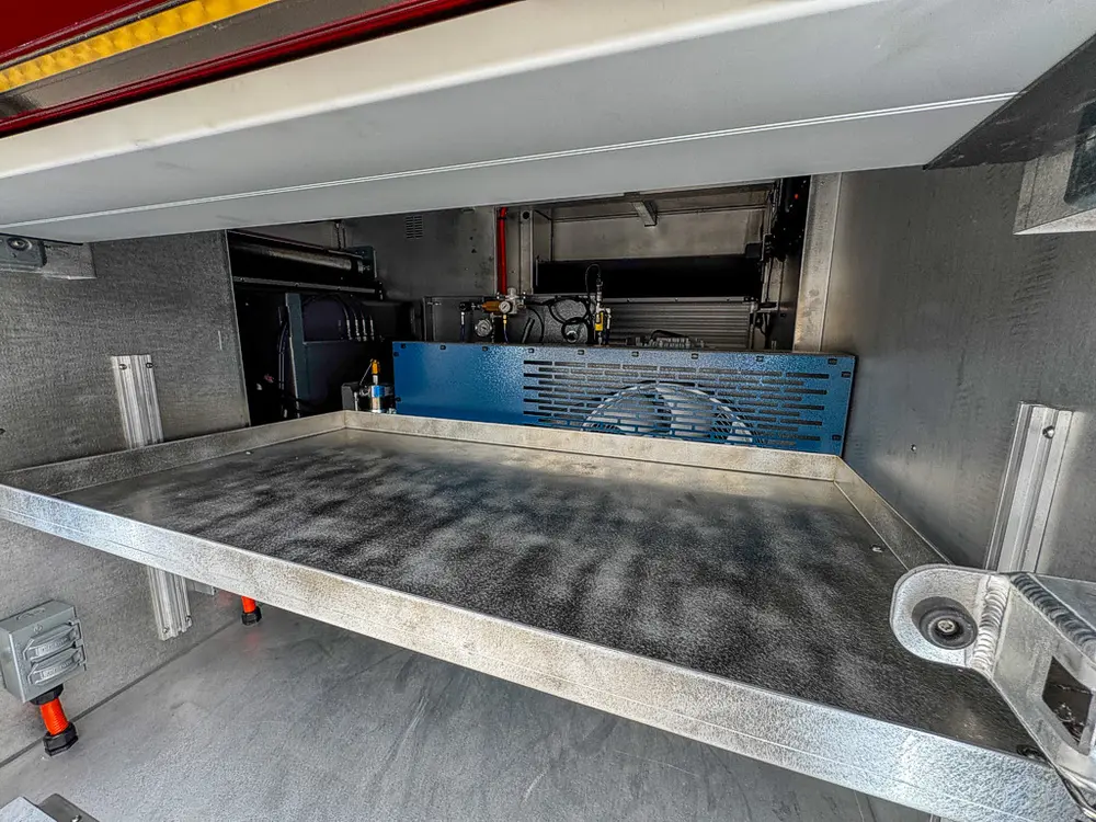 Exterior view of small fire truck showing cab, body compartments, and wheel/tire area.