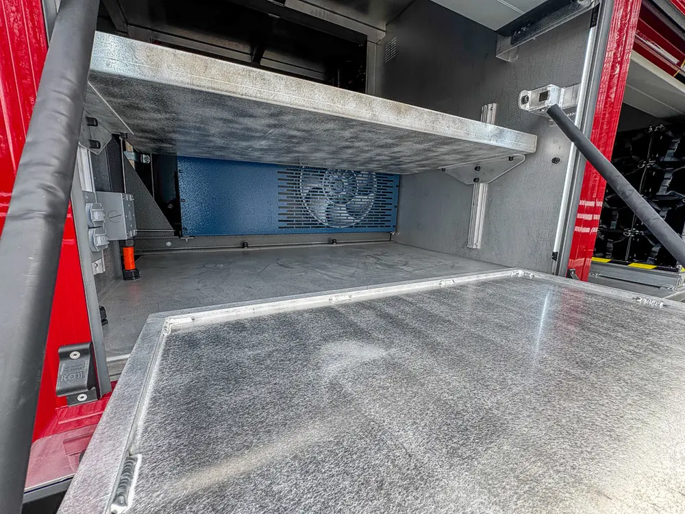 Exterior view of small fire truck showing cab, body compartments, and wheel/tire area.