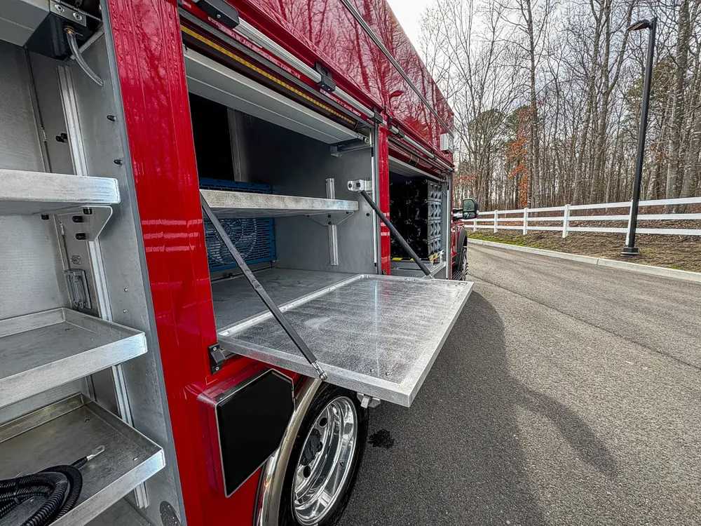 Exterior view of small fire truck showing cab, body compartments, and wheel/tire area.