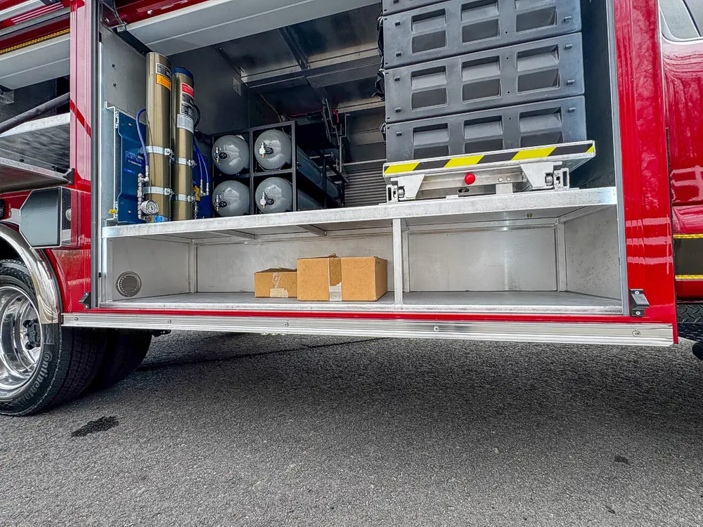 Exterior view of small fire truck showing cab, body compartments, and wheel/tire area.