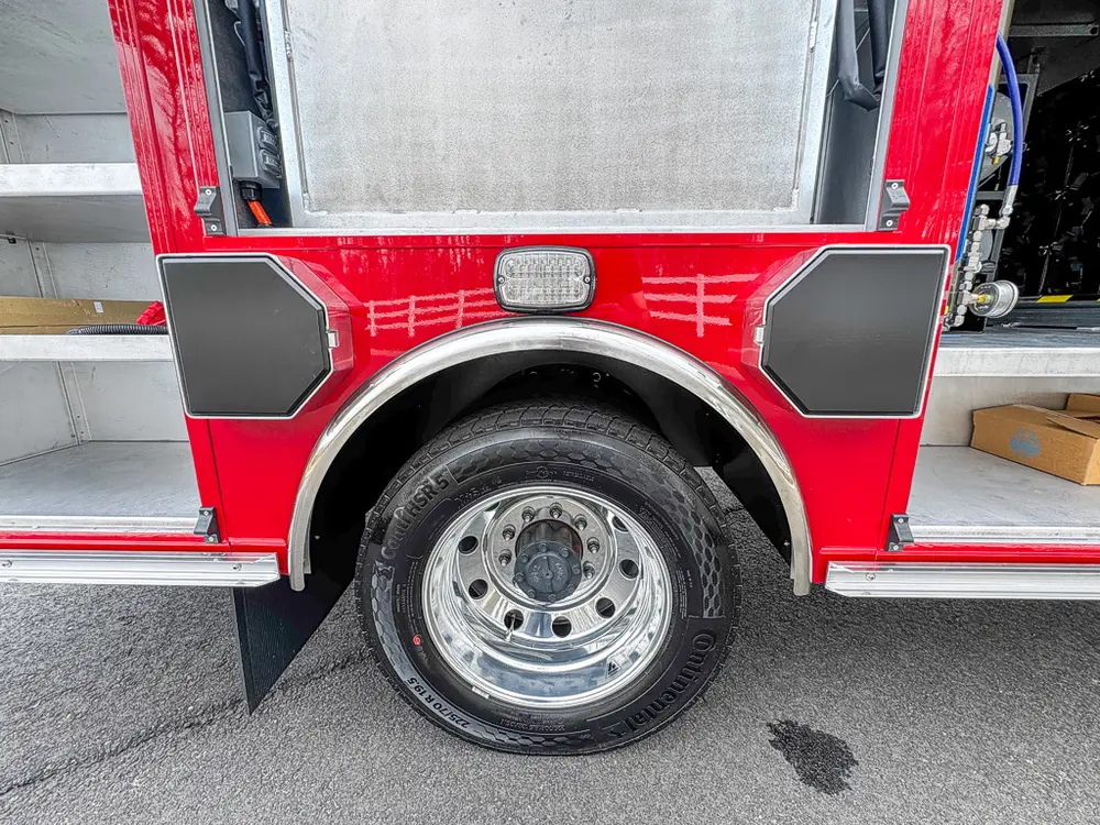 Exterior view of small fire truck showing cab, body compartments, and wheel/tire area.