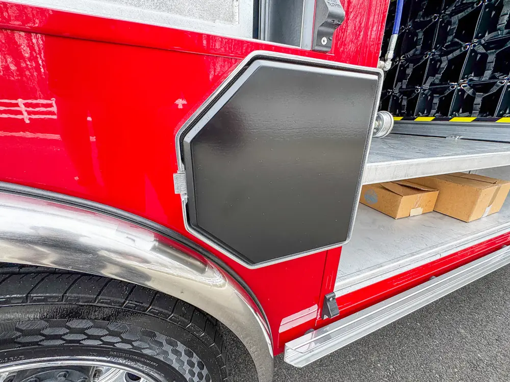 Exterior view of small fire truck showing cab, body compartments, and wheel/tire area.