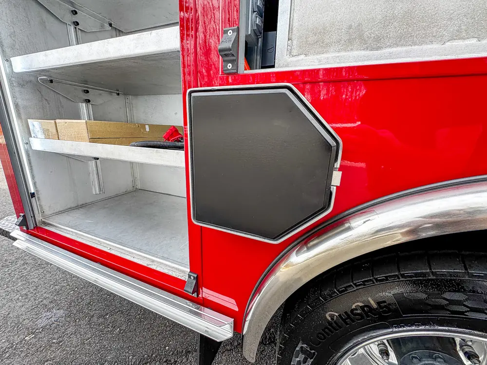 Exterior view of small fire truck showing cab, body compartments, and wheel/tire area.