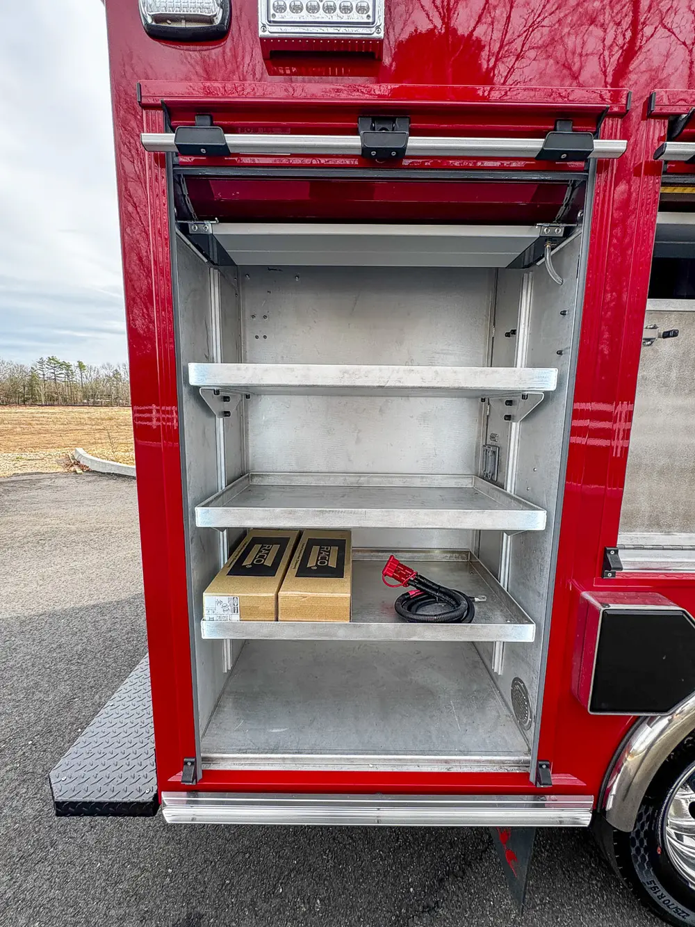 Exterior view of small fire truck showing cab, body compartments, and wheel/tire area.