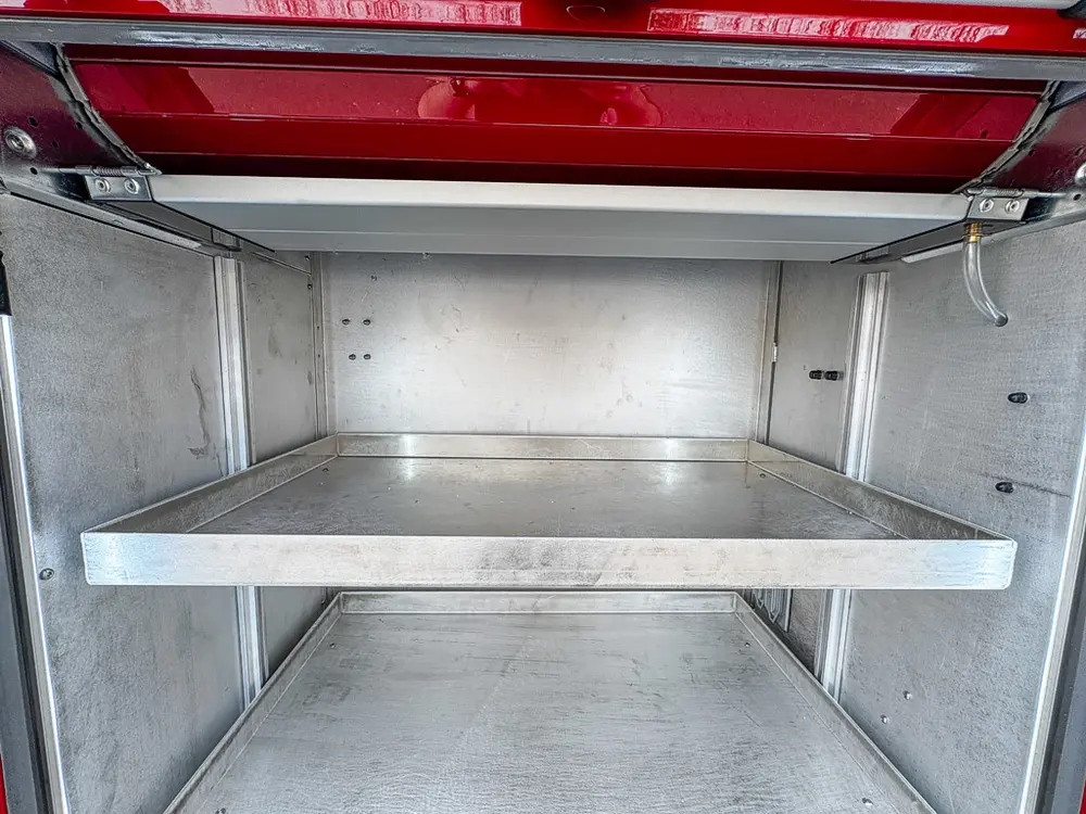 Exterior view of small fire truck showing cab, body compartments, and wheel/tire area.