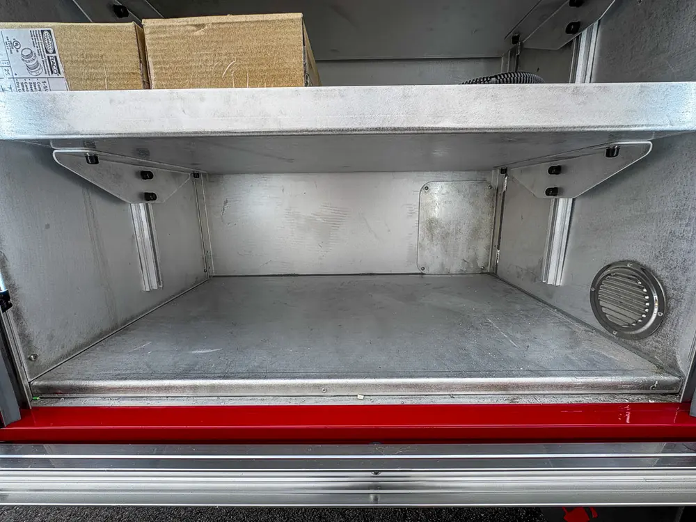 Exterior view of small fire truck showing cab, body compartments, and wheel/tire area.