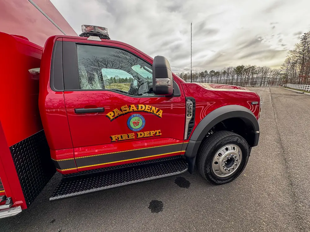 Exterior view of small fire truck showing cab, body compartments, and wheel/tire area.