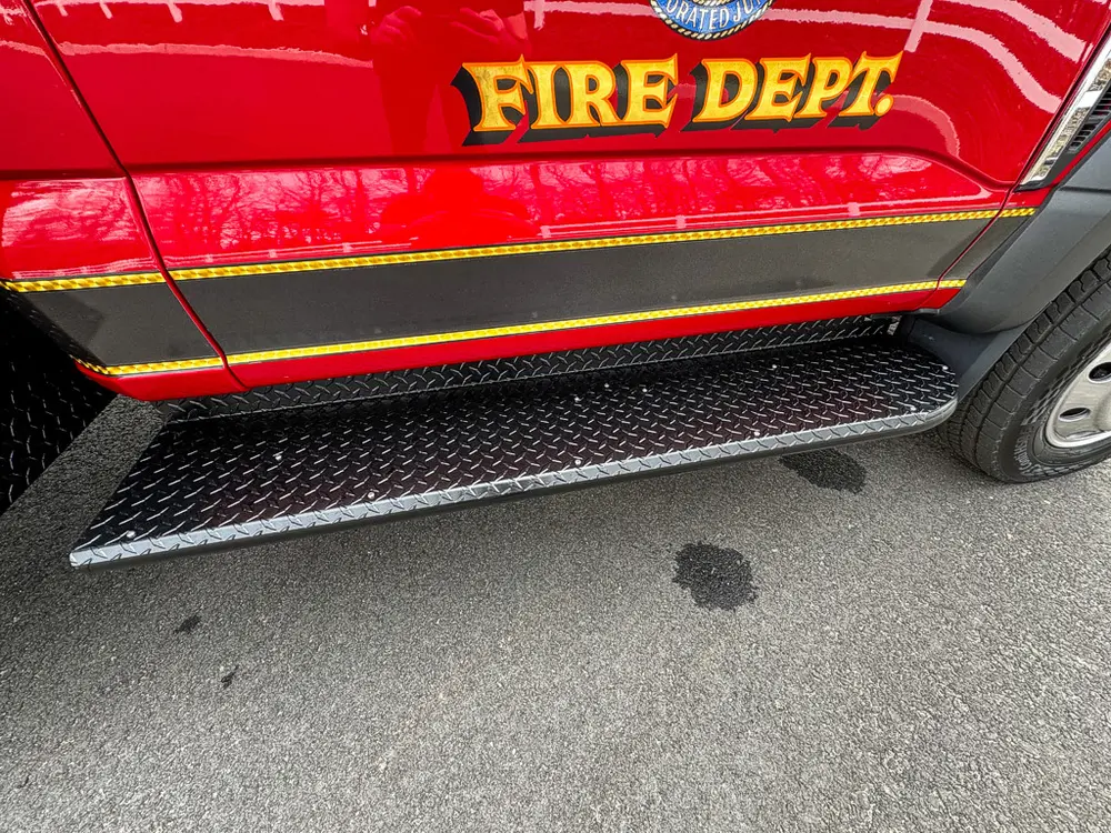 Exterior view of small fire truck showing cab, body compartments, and wheel/tire area.
