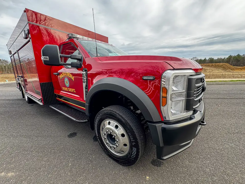 Exterior view of small fire truck showing cab, body compartments, and wheel/tire area.