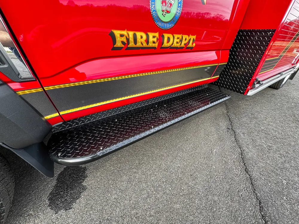 Exterior view of small fire truck showing cab, body compartments, and wheel/tire area.