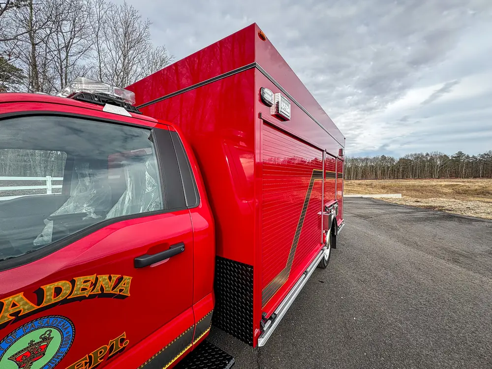Exterior view of small fire truck showing cab, body compartments, and wheel/tire area.
