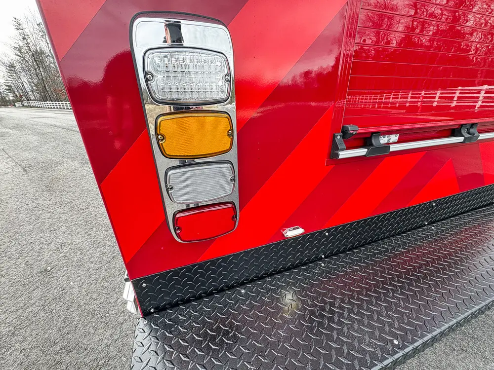 Exterior view of small fire truck showing cab, body compartments, and wheel/tire area.