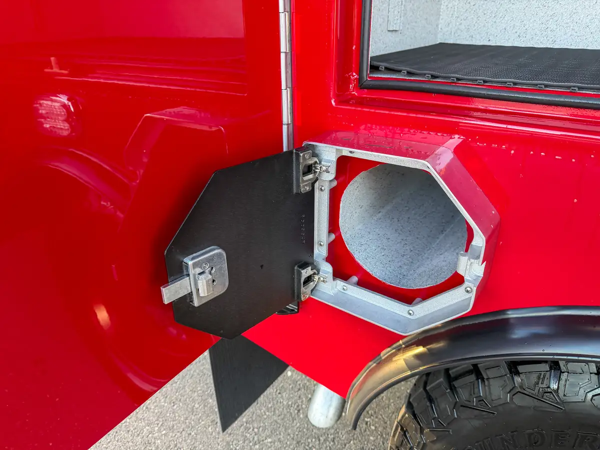 Close-up of open round utility port compartment beside rear wheel.