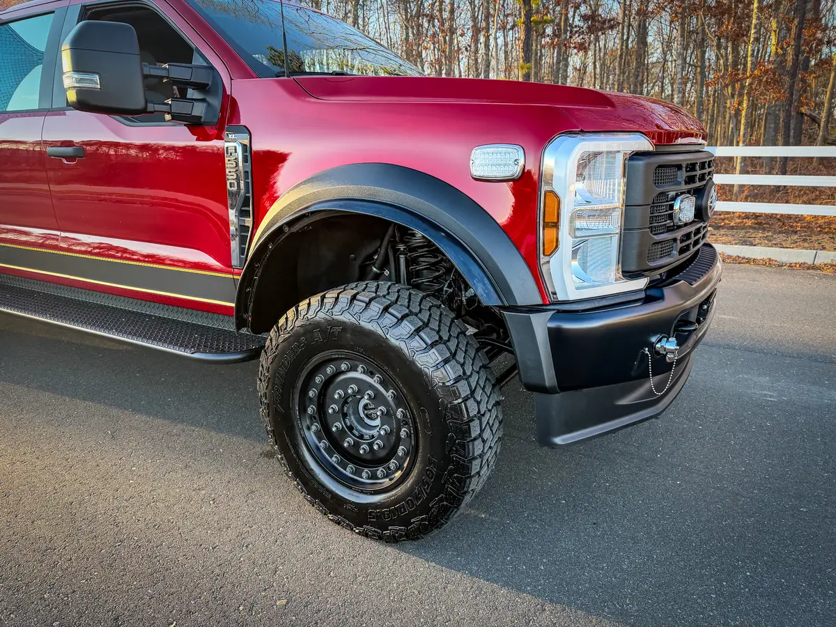 Front corner close-up showing headlight, bumper, and front wheel with off-road tire.
