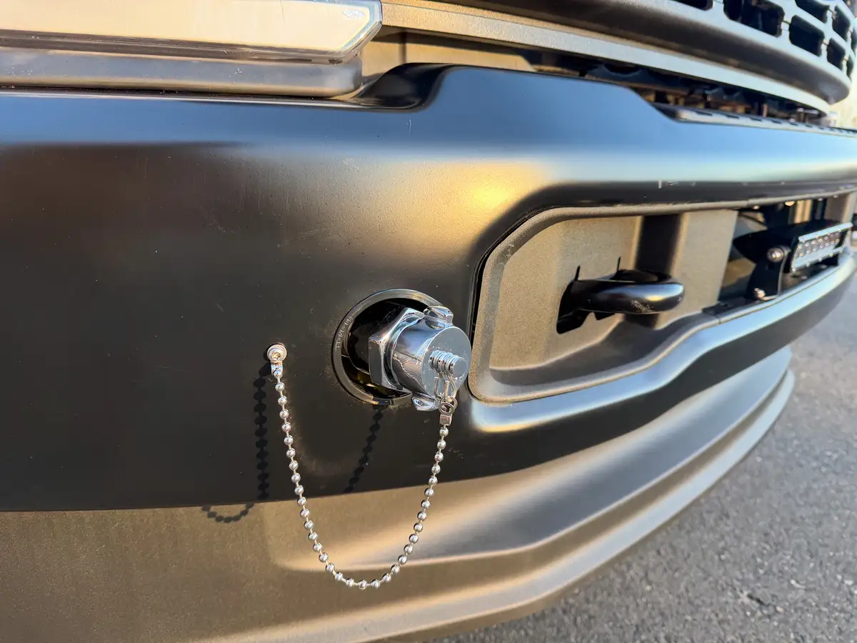 Tight close-up of front tow point with safety-cap chain on bumper.