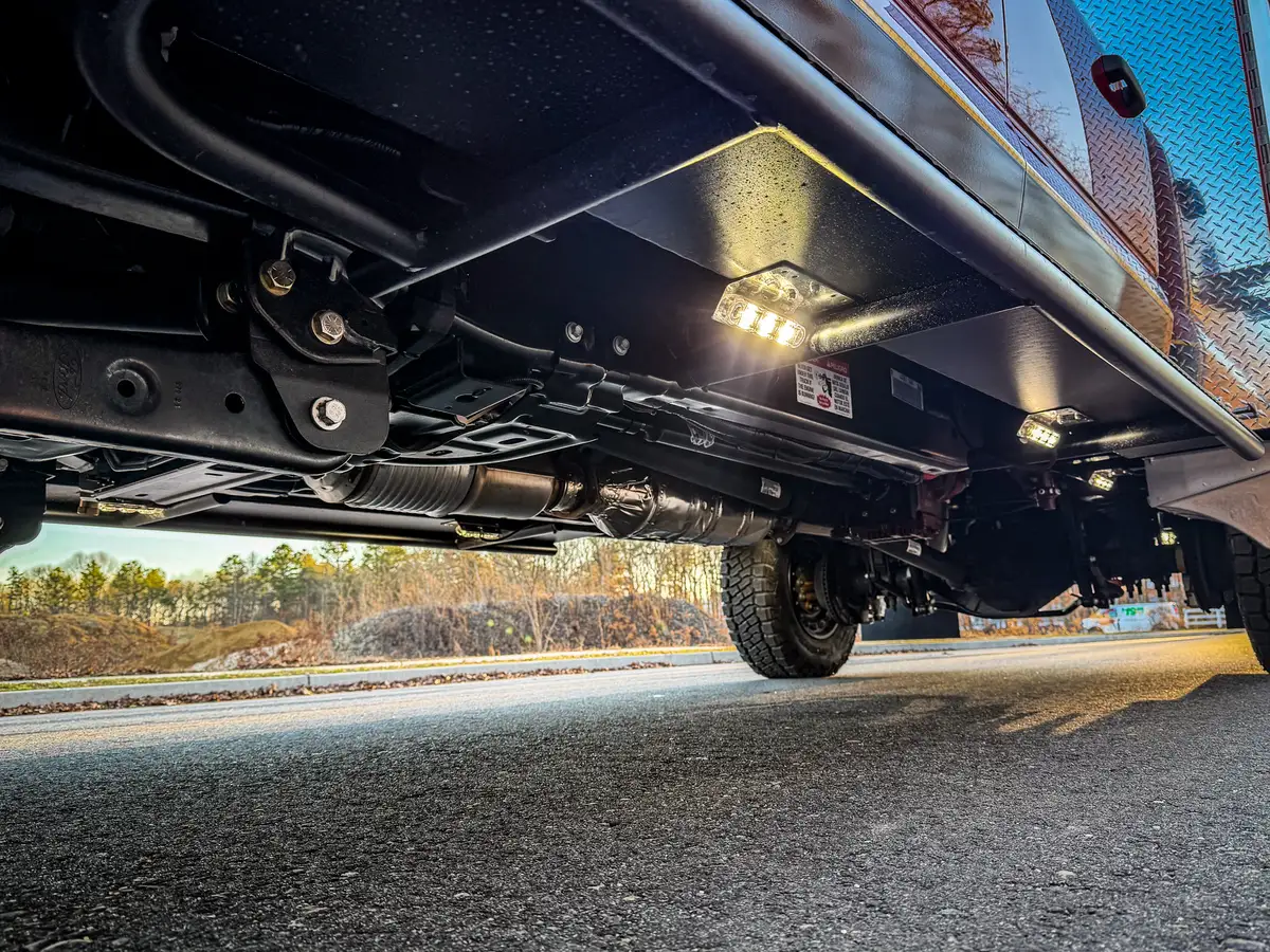 Low underbody view showing frame components and illuminated underside lights.