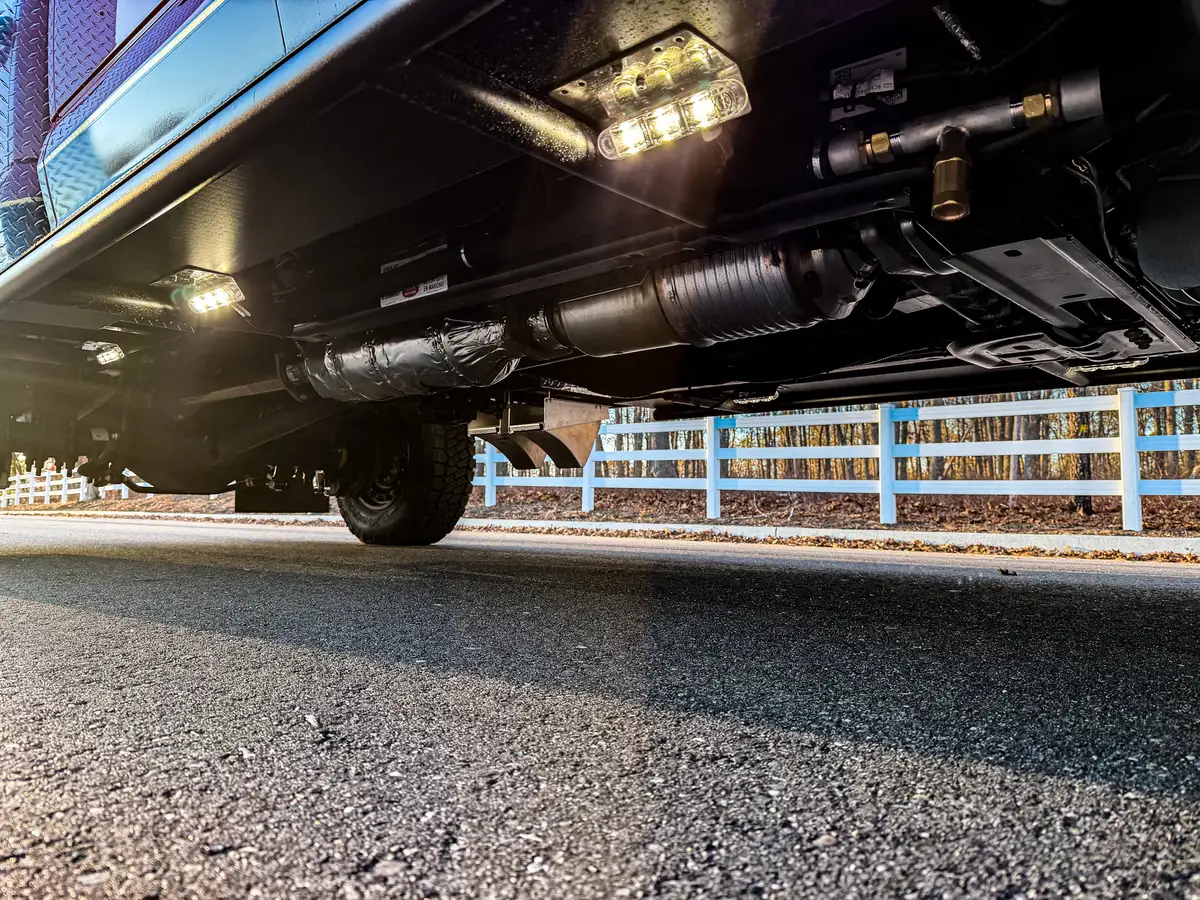 Underbody close-up from opposite side with illuminated lights and drivetrain components.