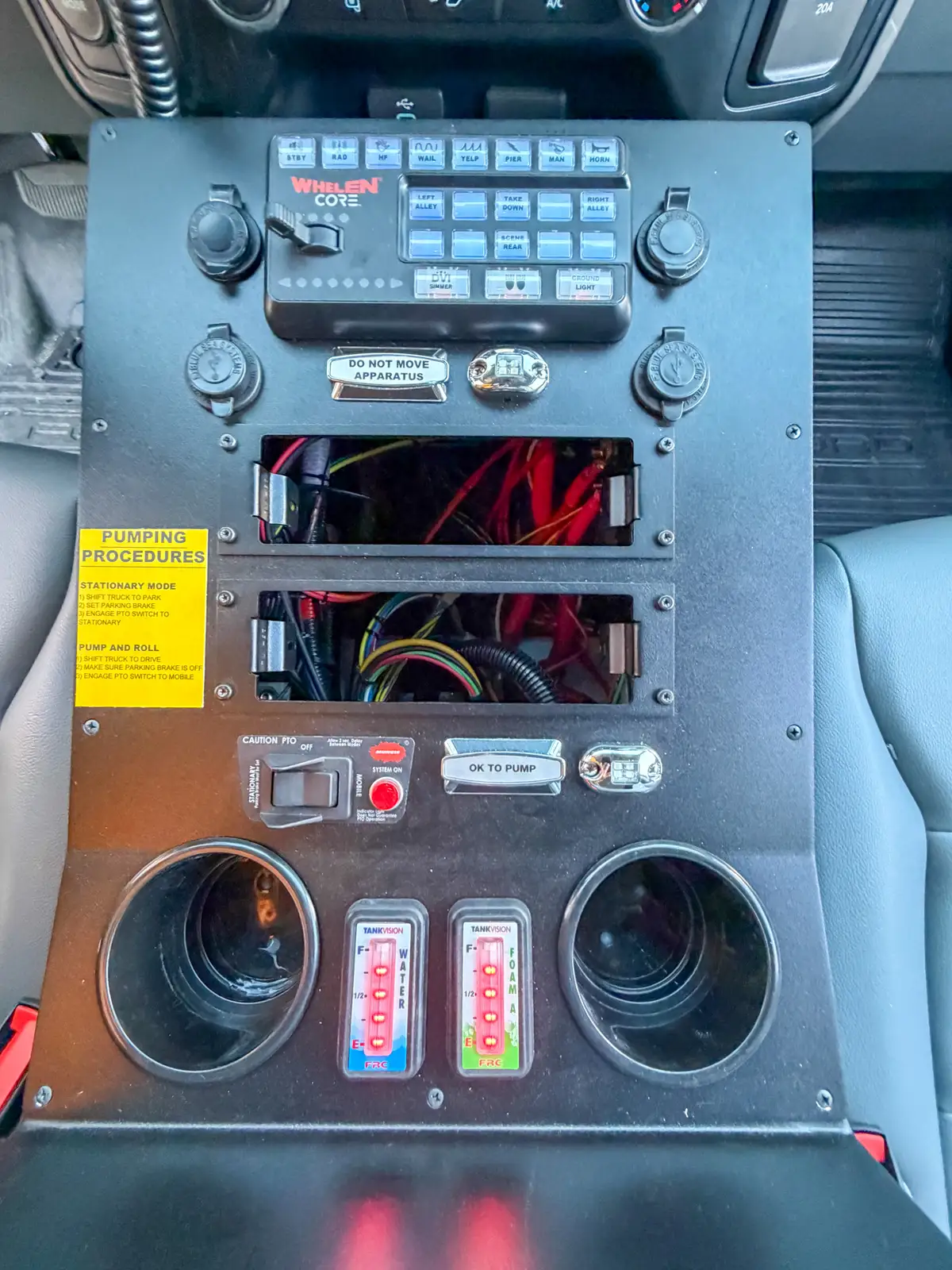 Top-down close-up of center console with switches, cup holders, and open wiring bays.