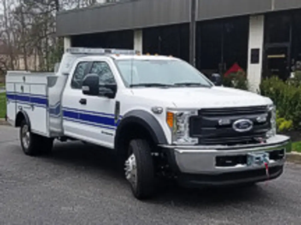Exterior view of small fire truck showing cab, body compartments, and wheel/tire area.