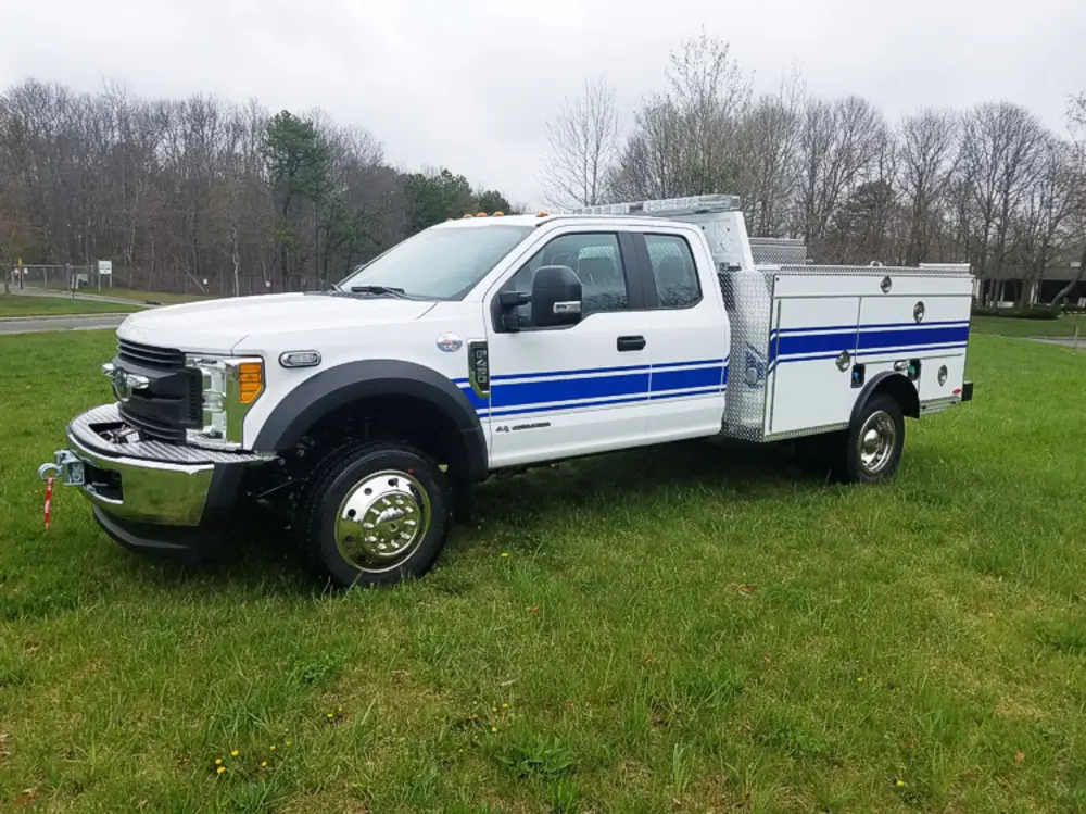 Exterior view of small fire truck showing cab, body compartments, and wheel/tire area.