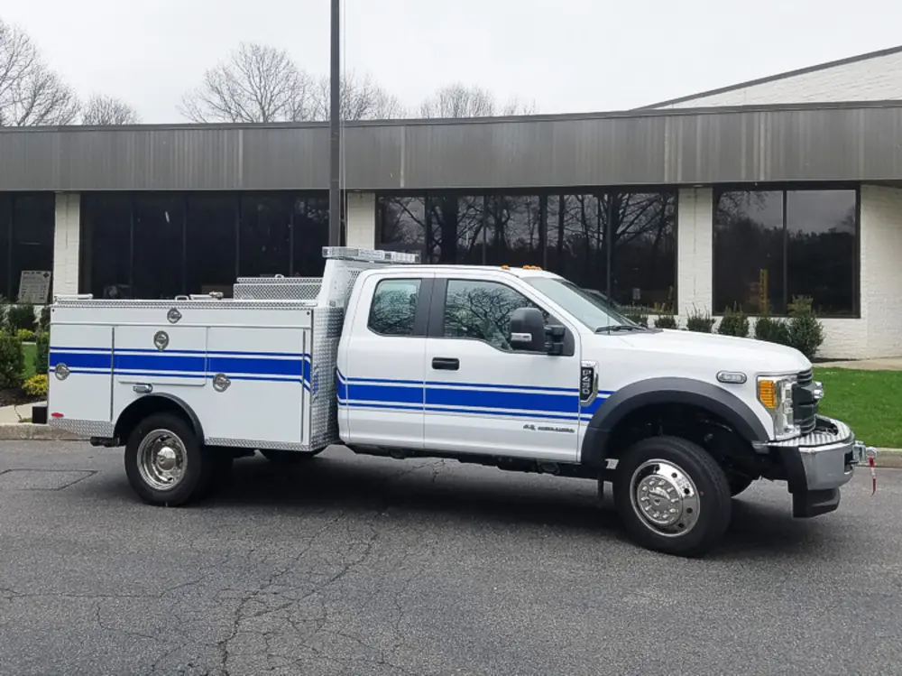 Exterior view of small fire truck showing cab, body compartments, and wheel/tire area.