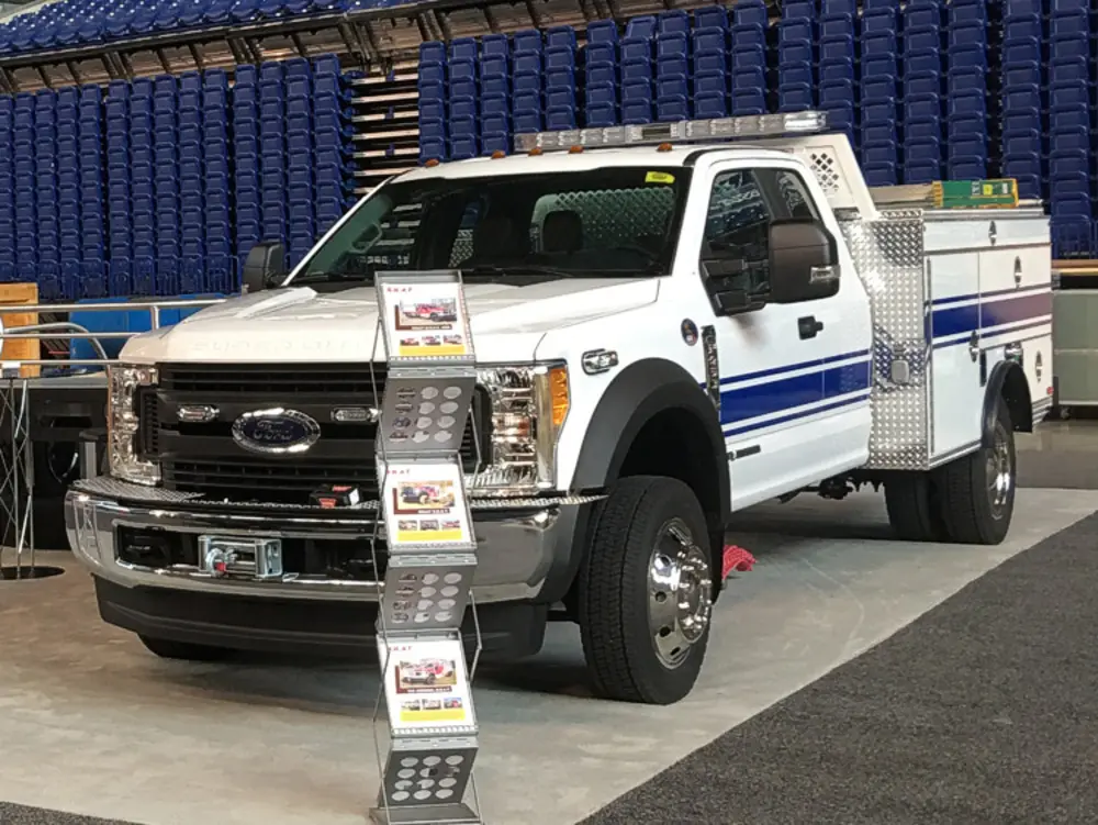 Exterior view of small fire truck showing cab, body compartments, and wheel/tire area.