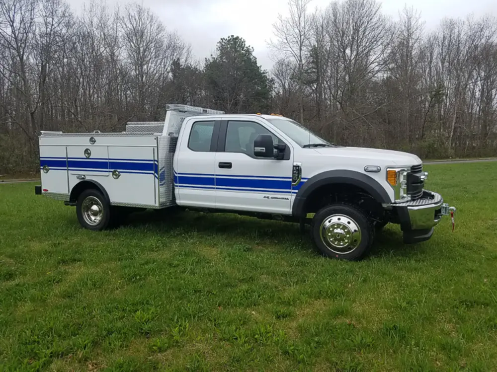 Exterior view of small fire truck showing cab, body compartments, and wheel/tire area.
