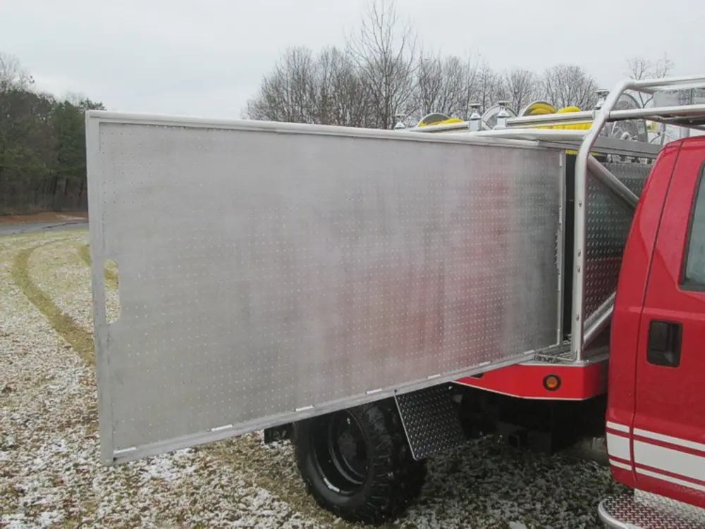 Exterior view of small fire truck showing cab, body compartments, and wheel/tire area.