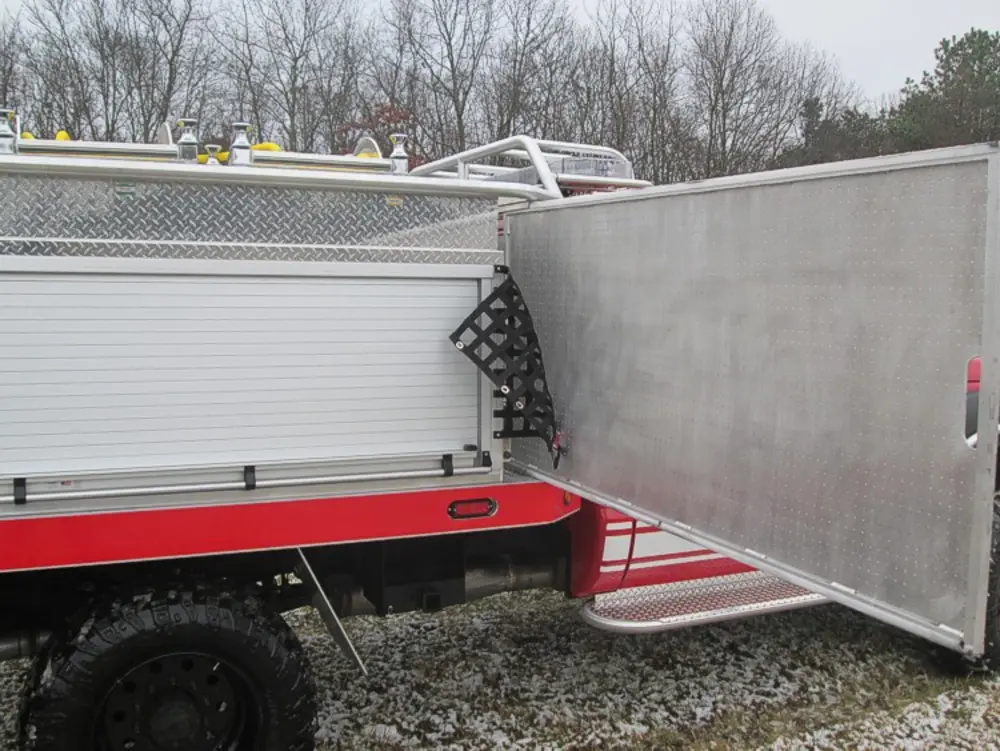 Exterior view of small fire truck showing cab, body compartments, and wheel/tire area.