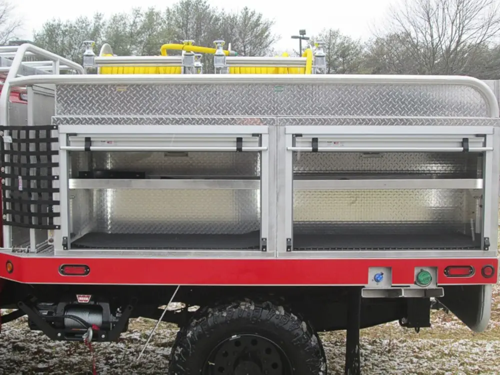 Exterior view of small fire truck showing cab, body compartments, and wheel/tire area.