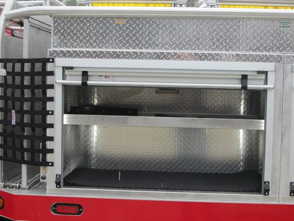 Exterior view of small fire truck showing cab, body compartments, and wheel/tire area.