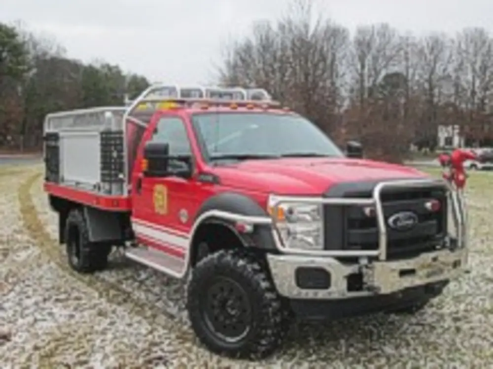 Exterior view of small fire truck showing cab, body compartments, and wheel/tire area.