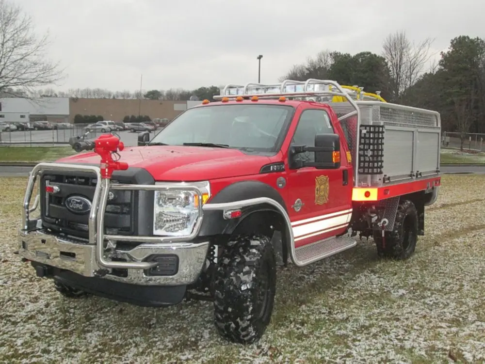 Exterior view of small fire truck showing cab, body compartments, and wheel/tire area.