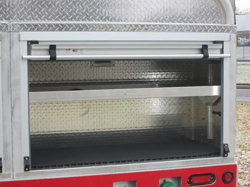 Exterior view of small fire truck showing cab, body compartments, and wheel/tire area.