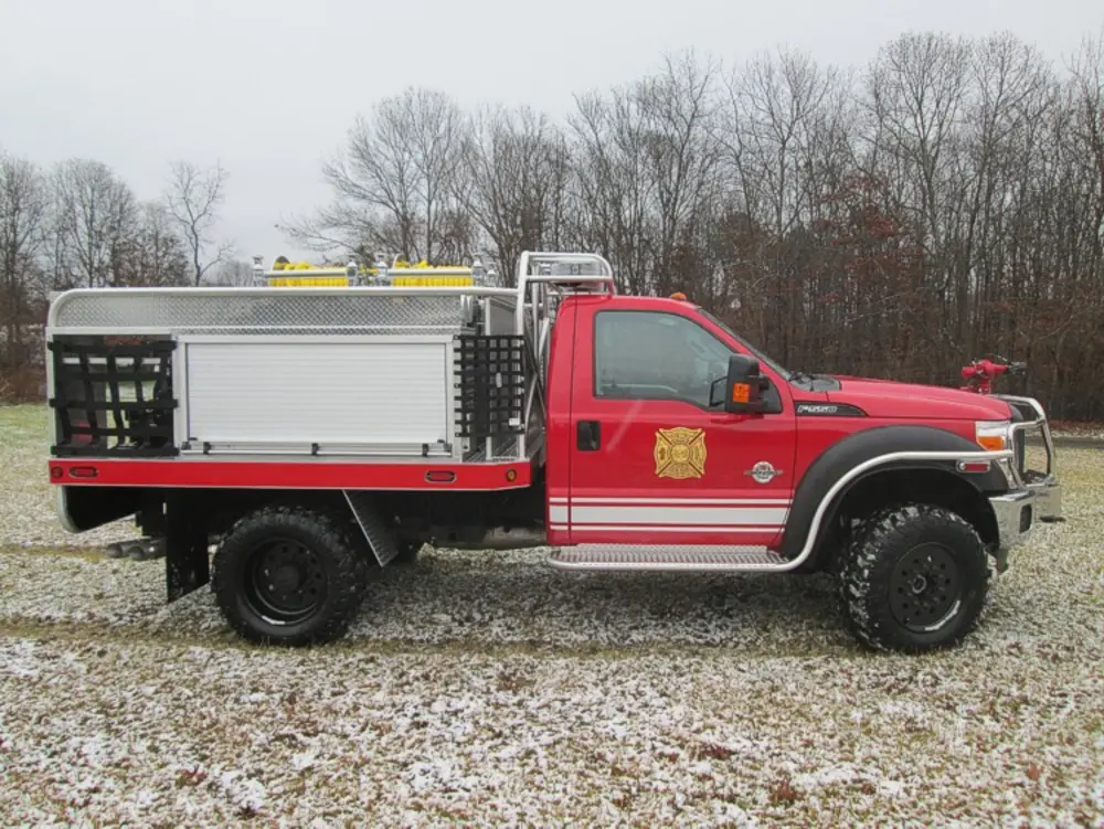 Exterior view of small fire truck showing cab, body compartments, and wheel/tire area.