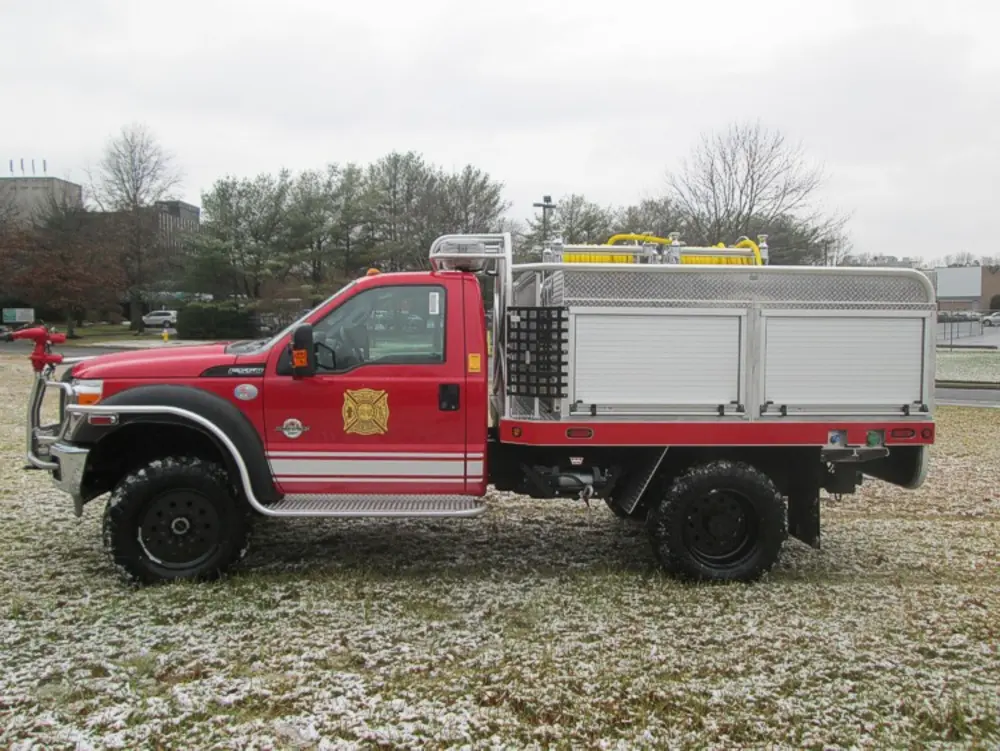 Exterior view of small fire truck showing cab, body compartments, and wheel/tire area.