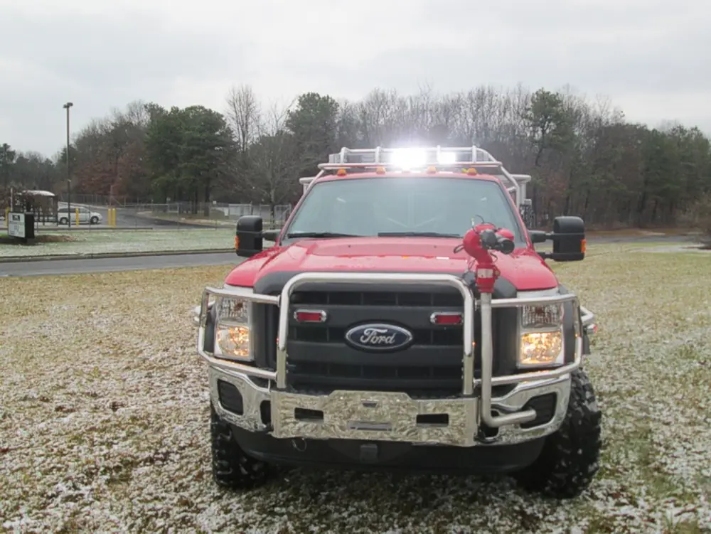 Exterior view of small fire truck showing cab, body compartments, and wheel/tire area.
