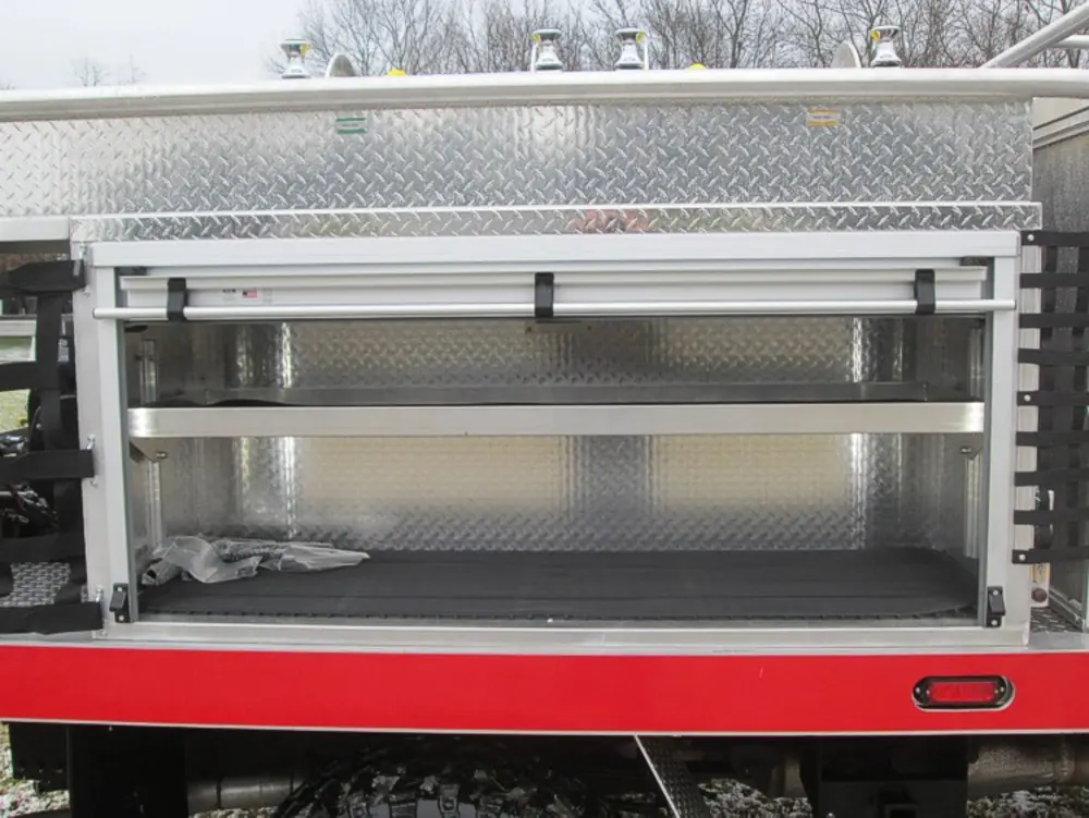 Exterior view of small fire truck showing cab, body compartments, and wheel/tire area.