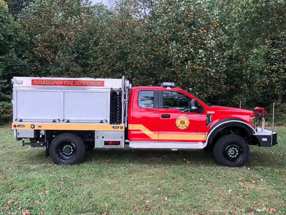 Exterior view of small fire truck showing cab, body compartments, and wheel/tire area.