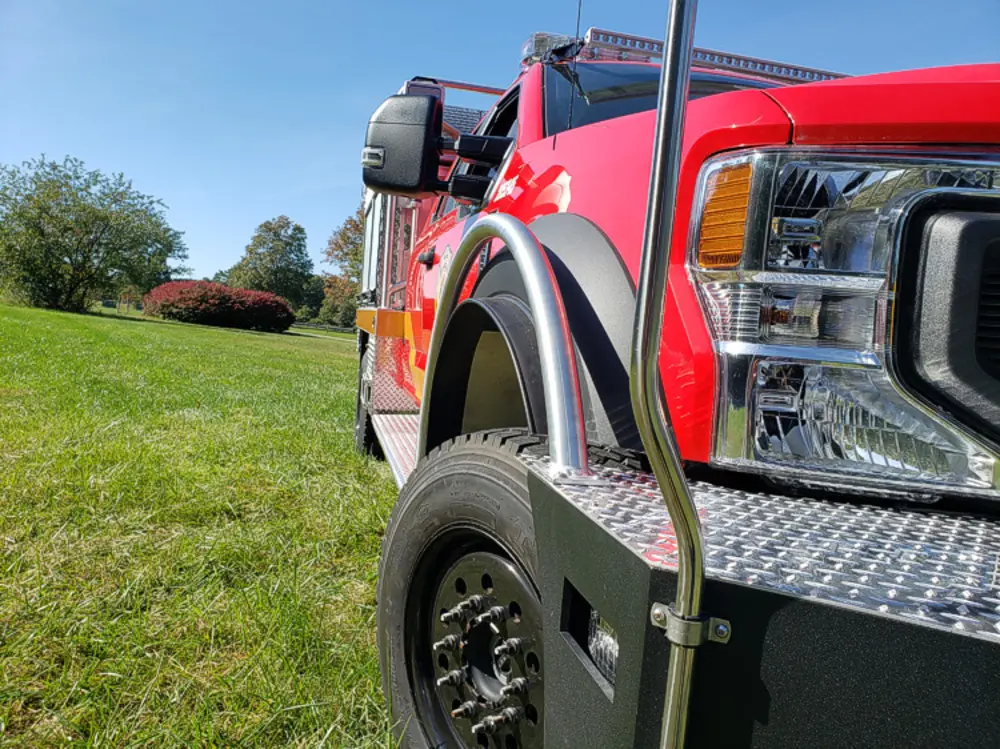 Exterior view of small fire truck showing cab, body compartments, and wheel/tire area.