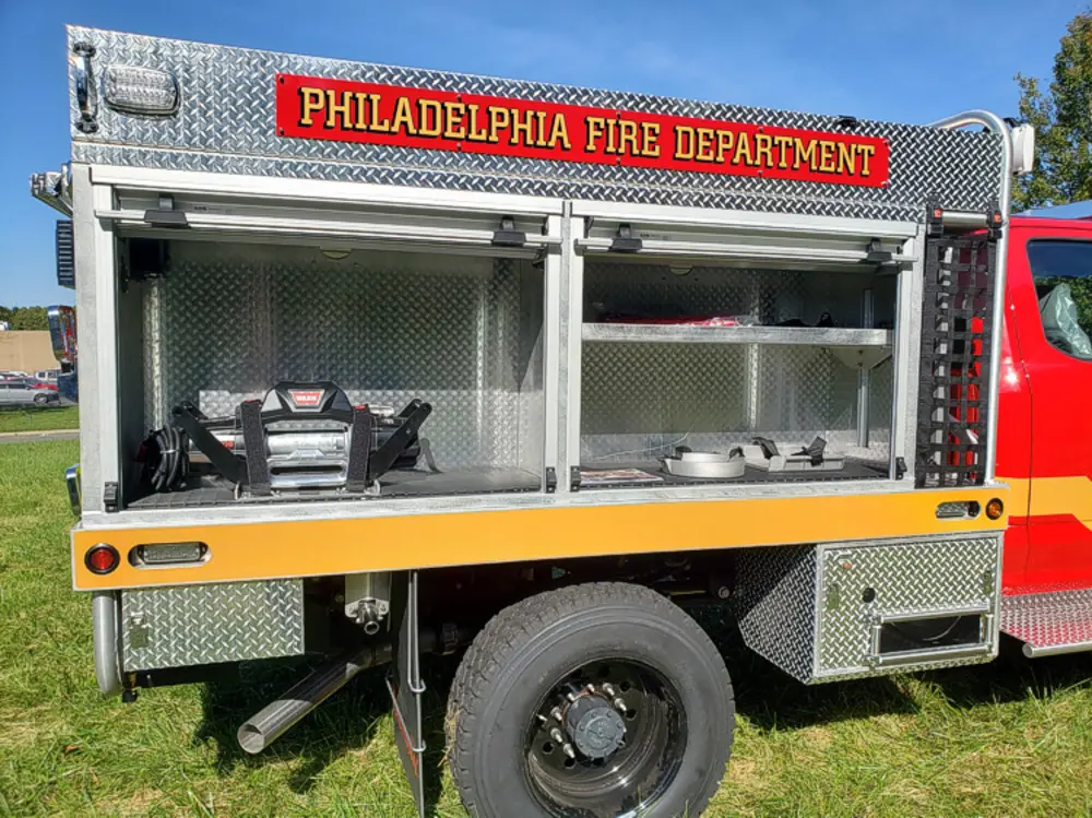 Exterior view of small fire truck showing cab, body compartments, and wheel/tire area.