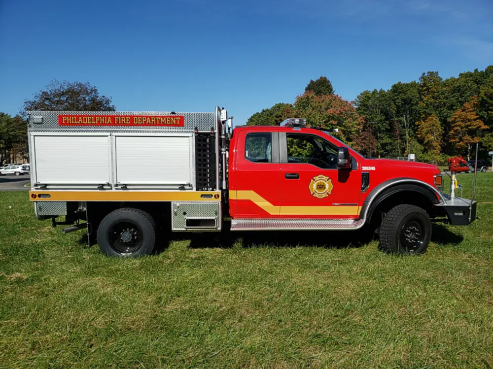 Exterior view of small fire truck showing cab, body compartments, and wheel/tire area.