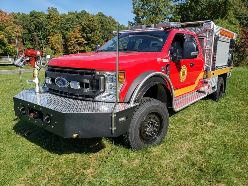 Exterior view of small fire truck showing cab, body compartments, and wheel/tire area.