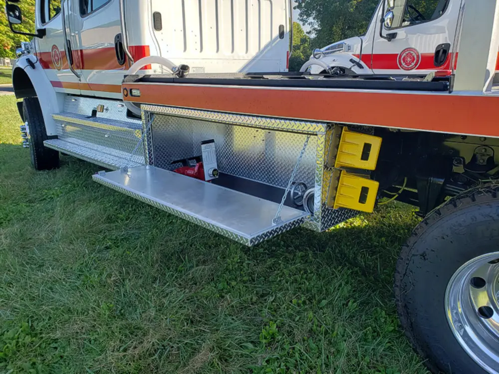 Exterior view of small fire truck showing cab, body compartments, and wheel/tire area.