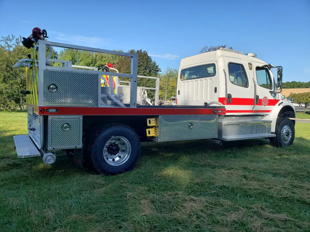 Exterior view of small fire truck showing cab, body compartments, and wheel/tire area.