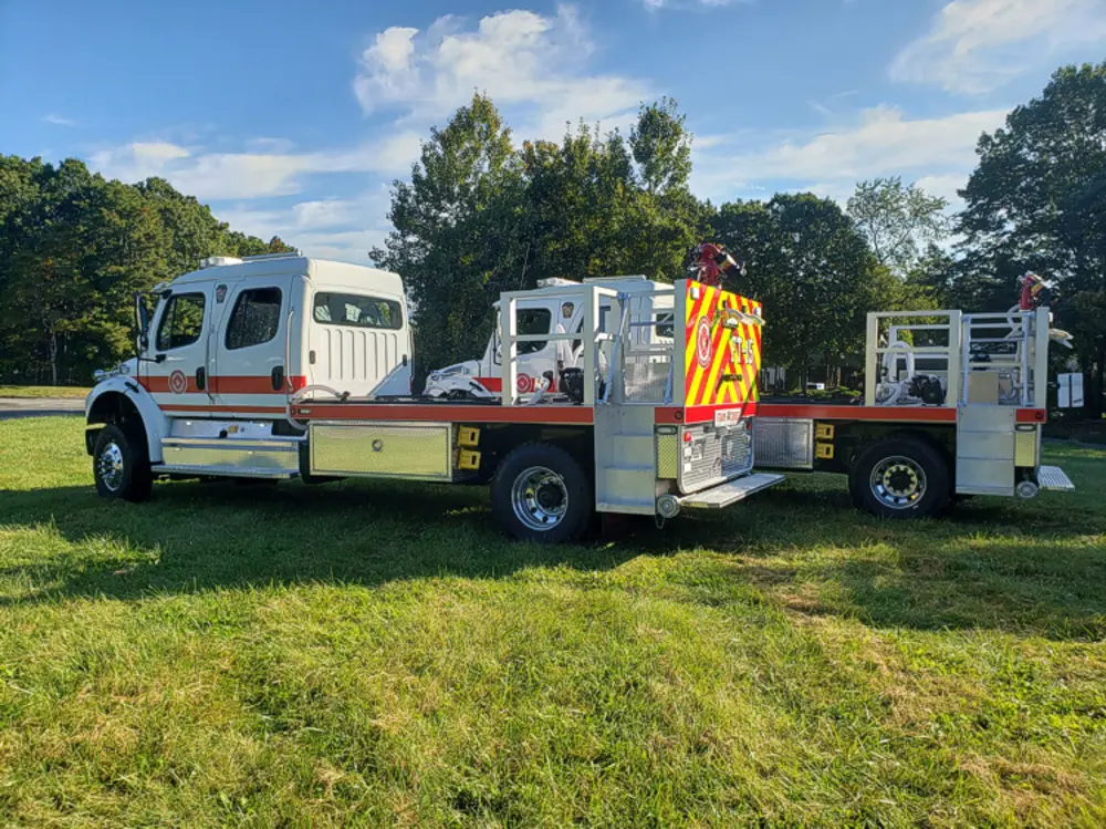 Exterior view of small fire truck showing cab, body compartments, and wheel/tire area.