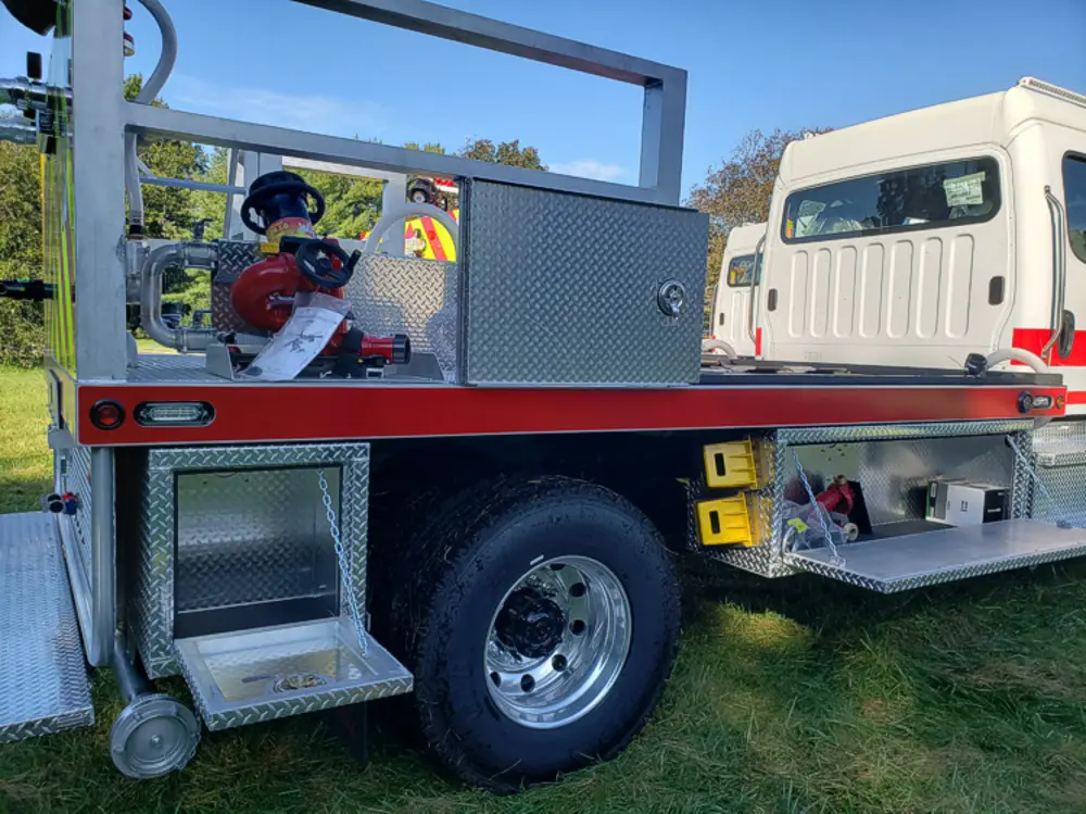 Exterior view of small fire truck showing cab, body compartments, and wheel/tire area.