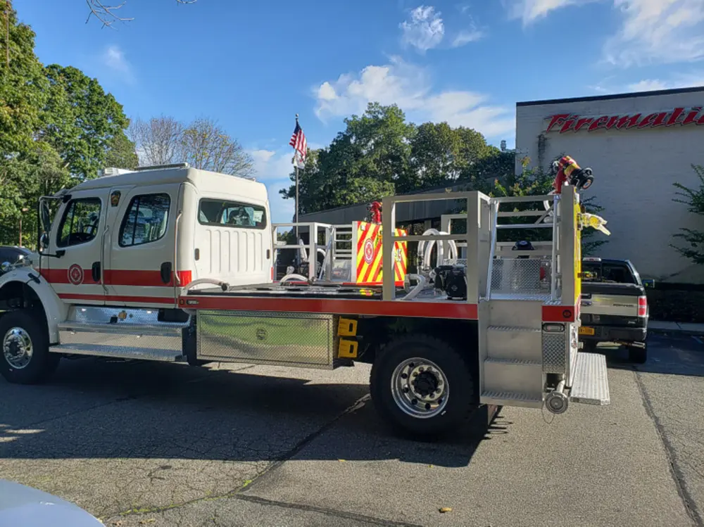 Exterior view of small fire truck showing cab, body compartments, and wheel/tire area.